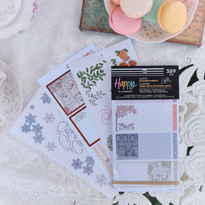 A set of Happy Planner sticker sheets and decorative stickers displayed on a white lace tablecloth, styled with pastel macarons in the background.