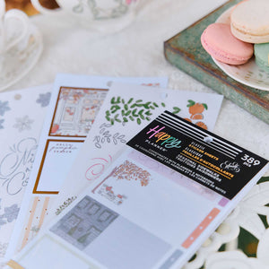 A package of D. La Beige Classic Planner Sheets with autumn-themed designs, fanned out on a white tablecloth next to macarons and a teacup.