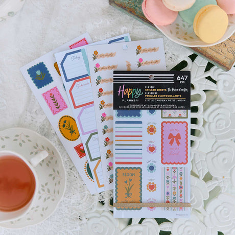 Little Garden sticker book and colourful floral sheets on a white table beside tea and macarons