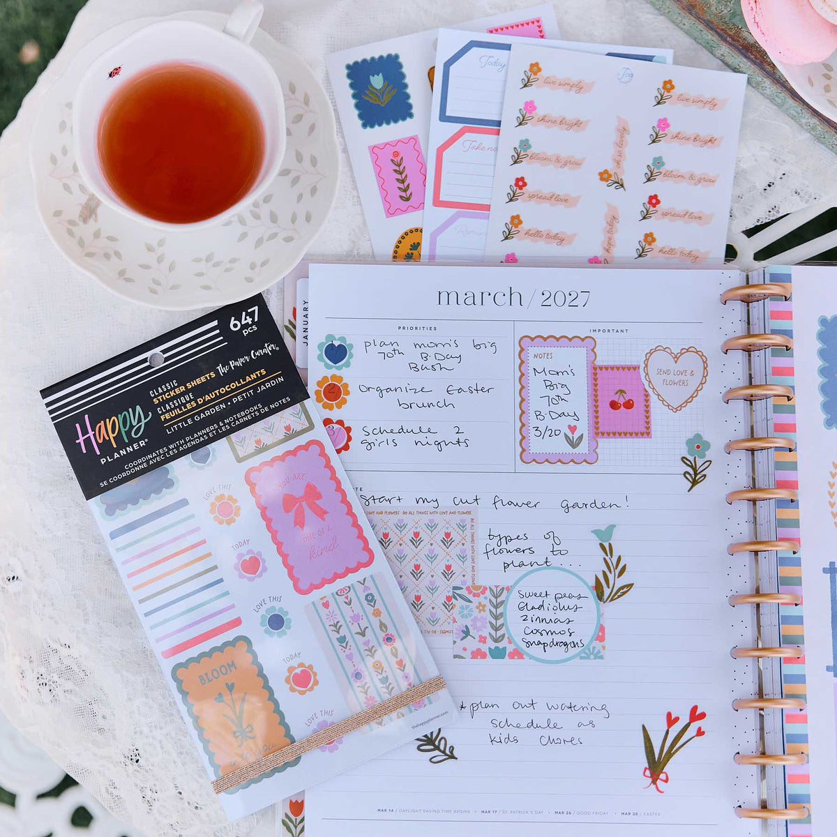 Little Garden sticker book and sheets beside tea and an open planner decorated with flowers, hearts and boxes