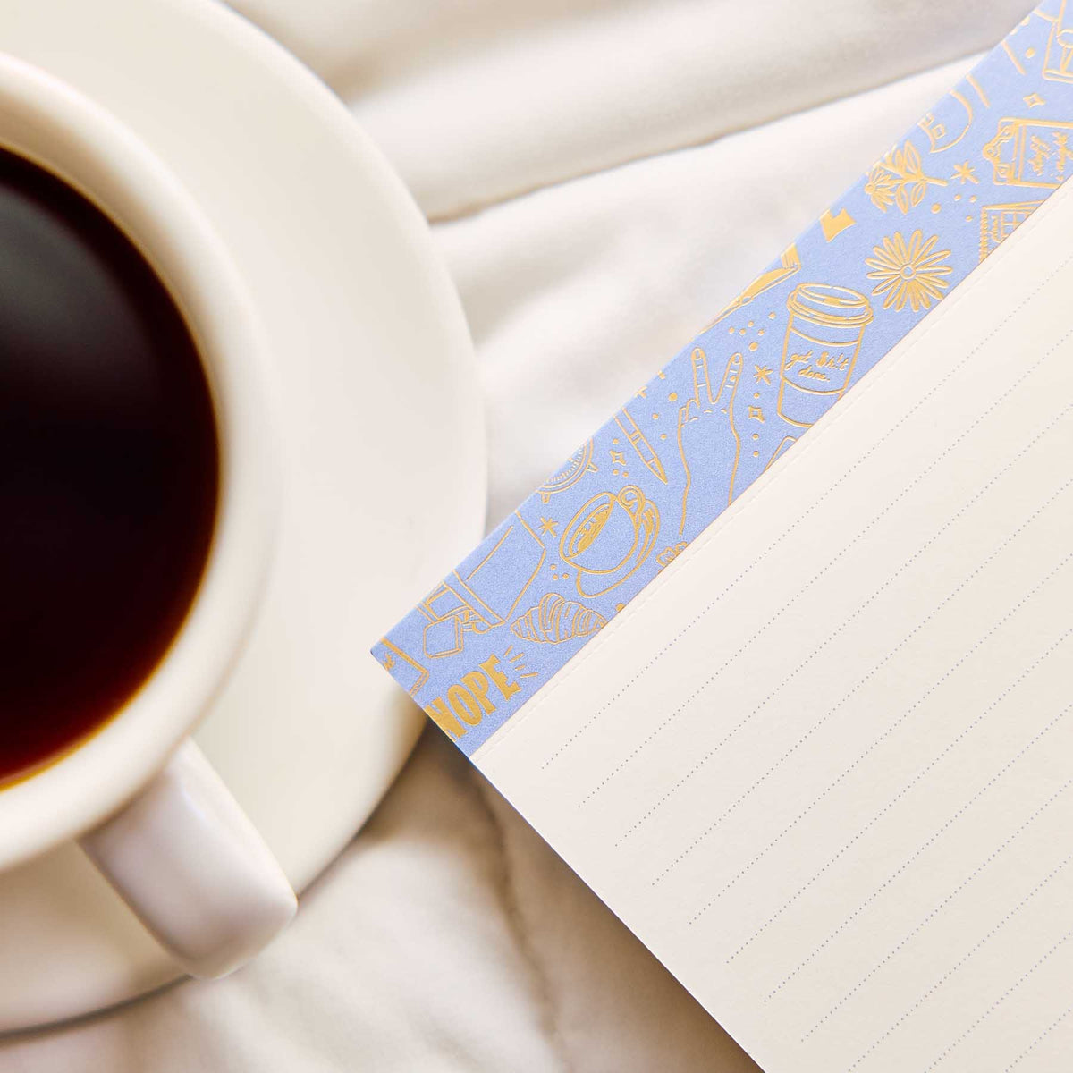 Pajama Plans notepad with a blue and gold border beside a coffee cup