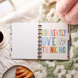 Open Pajama Plans notebook with Currently Overthinking artwork beside coffee and a croissant