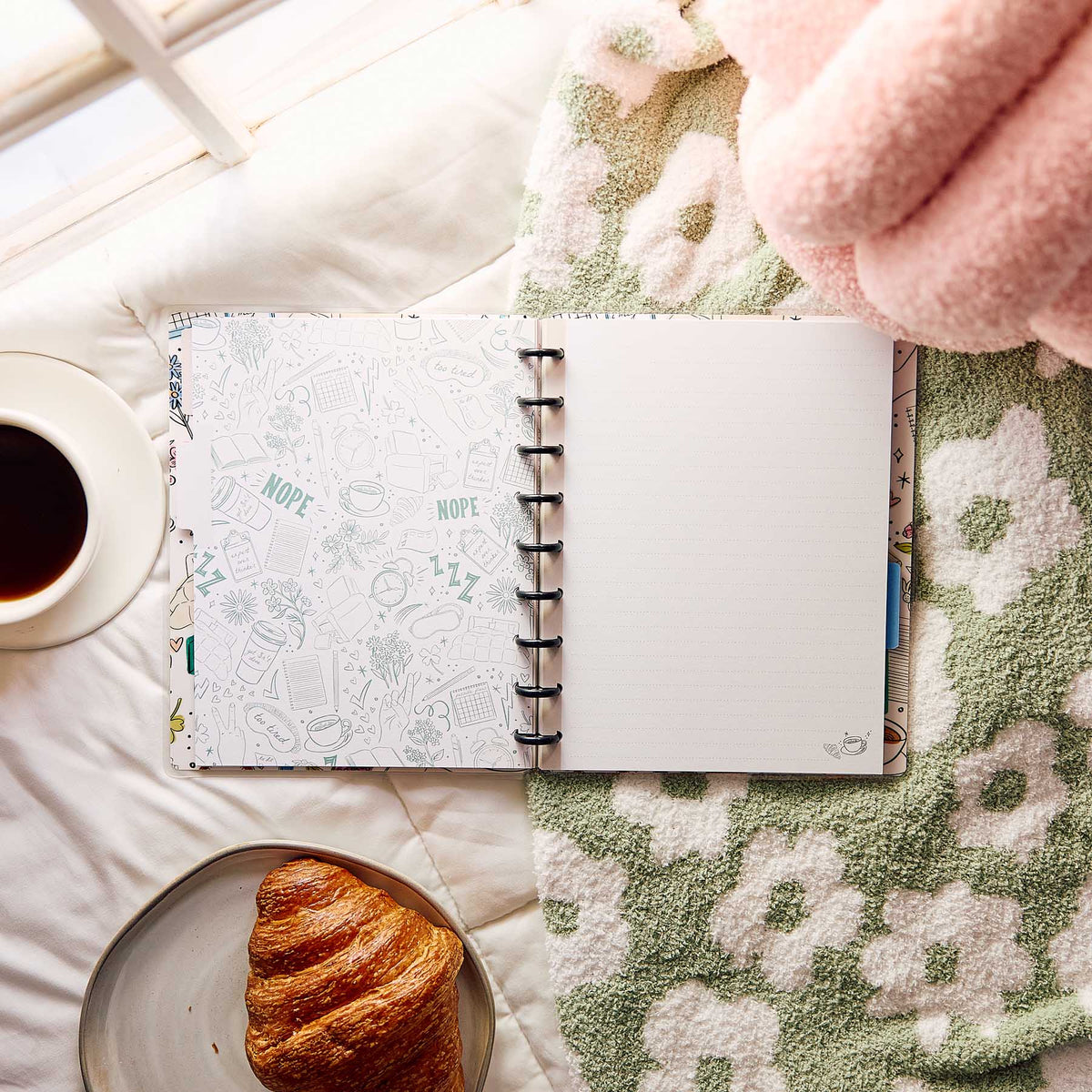 Open Pajama Plans notebook on a blanket beside coffee and a croissant