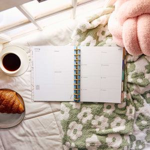 Pajama Plans Big disc-bound planner beside coffee and a croissant on a bed