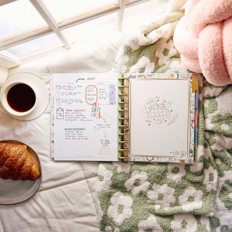 Pajama Plans Big planner with handwritten plans beside coffee and a croissant