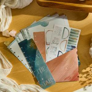 Starlit Glow celestial sticker sheets and starry inserts on a wooden surface