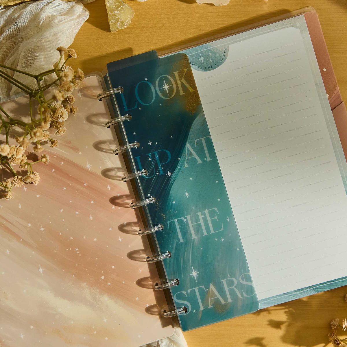 Starlit Glow celestial planner with lined filler paper beside dried flowers