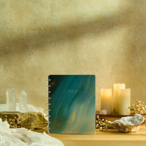Starlit Glow notebook with a teal marbled cover beside candles and crystals
