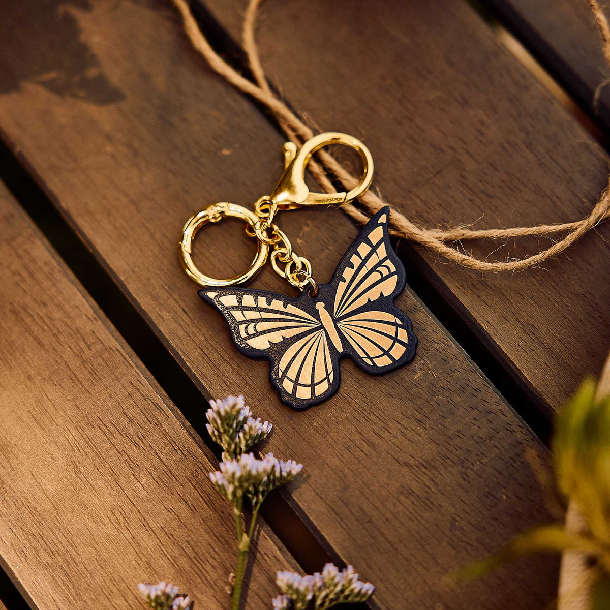 Dark blue and gold Butterfly Planner Charm resting on a wooden table beside small flowers