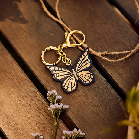 Dark blue and gold Butterfly Planner Charm resting on a wooden table beside small flowers