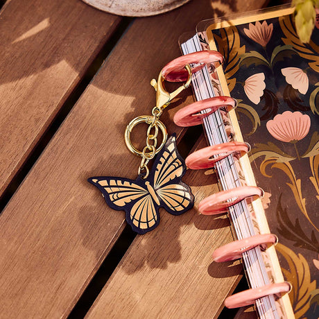 Butterfly Planner Charm hanging from a pink disc on a floral Happy Planner