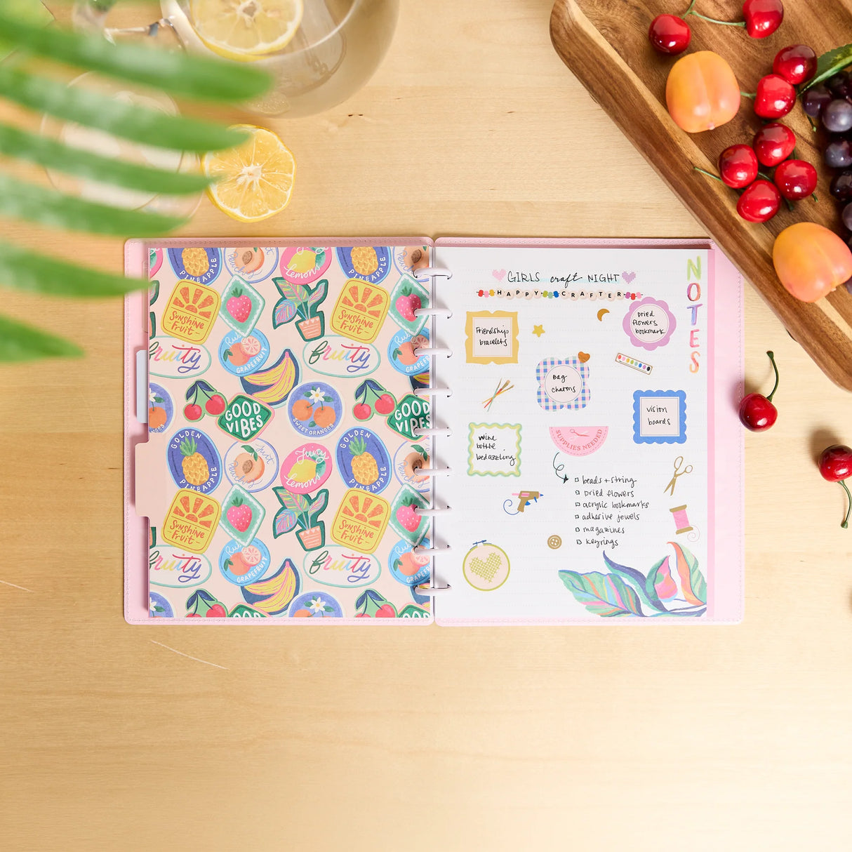 Open notebook with decorative stickers on a wooden surface with fruits and a glass of lemonade.