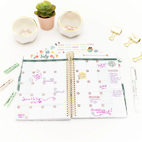 Open planner with July monthly view on a white surface with decorative items