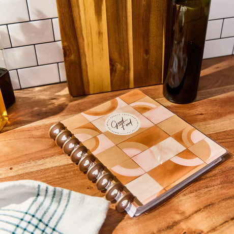 Recipe Keeper with a geometric cover on a wooden surface next to a bottle and cutting board.