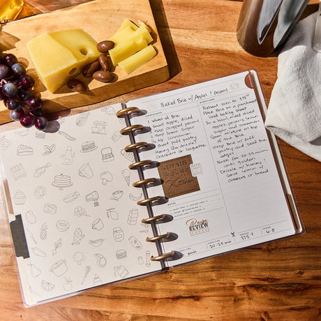 Open recipe notebook on a wooden surface with food items in the background