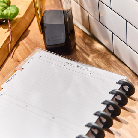 Open planner on a wooden surface with a bottle and plant in the background