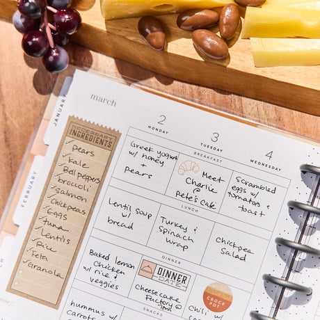 Calendar with meal planning notes on a wooden table with cheese and grapes.
