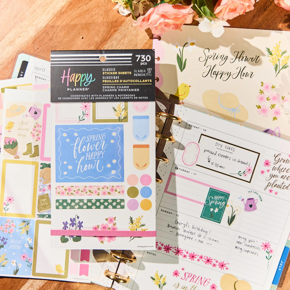 Happy Planner Spring Charm Classic Sticker Book collection planner stickers and sheets on a wooden surface with flowers.