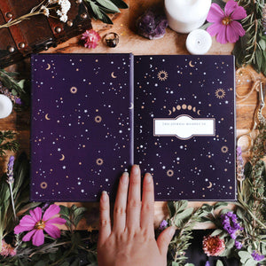 Open notebook with celestial design on a wooden surface with flowers and candles