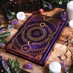 Purple book with gold designs on a wooden surface with candles and crystals