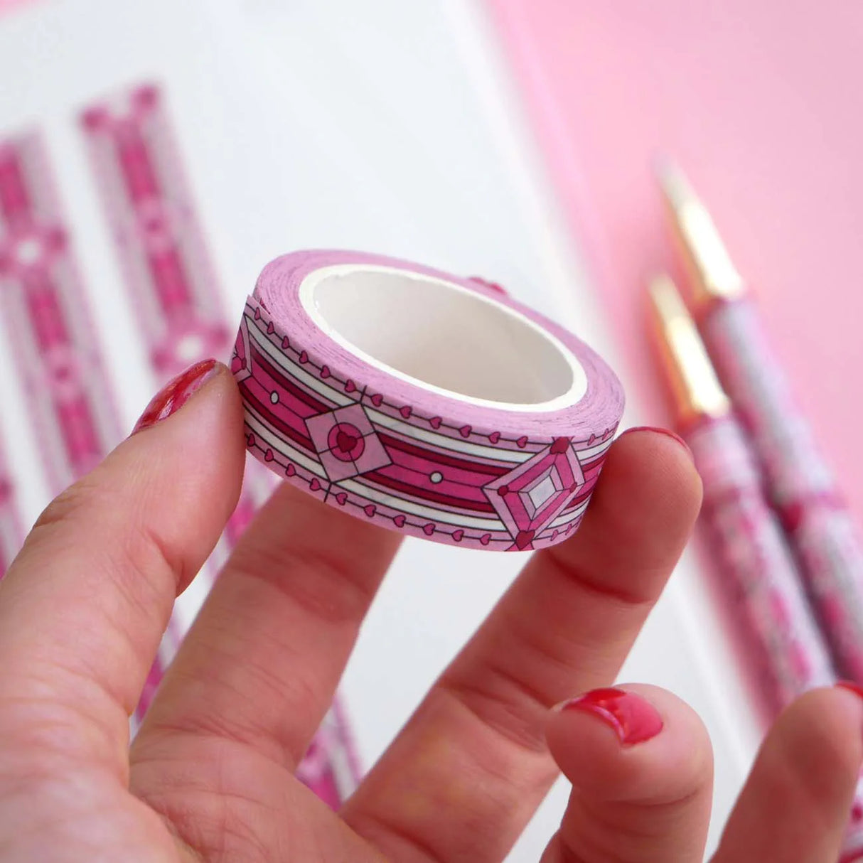 Hand holding a roll of pink decorative tape with geometric patterns on a blurred background.