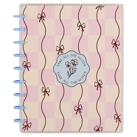 Notebook with decorative cover featuring ribbons and a logo on a pink and beige checkered background.